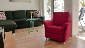 A modern living room with a green sofa, a red armchair, and a glass coffee table with a vase of flowers. - Strandglück Apartment 15C - Strandglück House C (Scharbeutz)