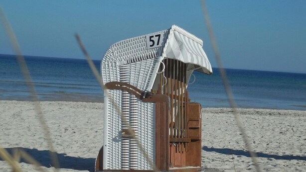 A beach chair with the number 57, a white striped umbrella, and a wooden bench. - Strandglück Apartment 15C - Strandglück House C (Scharbeutz)