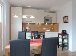 Una cocina moderna con armarios blancos, microondas, cafetera y comedor con mesa y sillas.