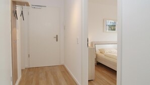 A hallway leading to a bedroom with a bed, a door, and a coat rack. - Strandglück Apartment 15C - Strandglück House C (Scharbeutz)