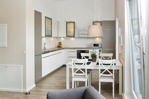 A modern kitchen with white cabinets, a dining area with white chairs, and a grey sofa.