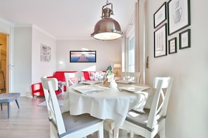 A dining area with a round table set for four, white chairs, and a red sofa in the background. - Strandglück Apartment 8C - Strandglück House C (Scharbeutz)