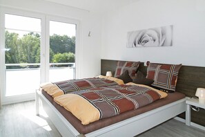 Een moderne slaapkamer met een groot bed, uitzicht op het groen via een schuifdeur en een schilderij aan de muur.
