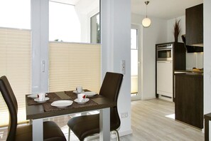 Een moderne keuken met een ingebouwde oven en magnetron, een eethoek met een tafel gedekt voor vier personen, en een groot raam dat zorgt voor natuurlijk licht.