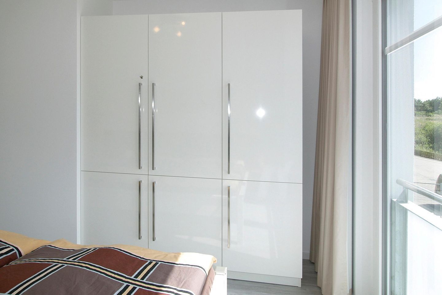 A bedroom with a bed, a large wardrobe, and a window with curtains.