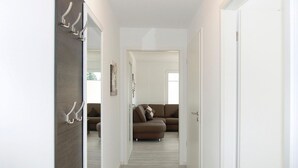 Corredor que dá para uma sala de estar com um sofá marrom e uma porta com espelho e ganchos.