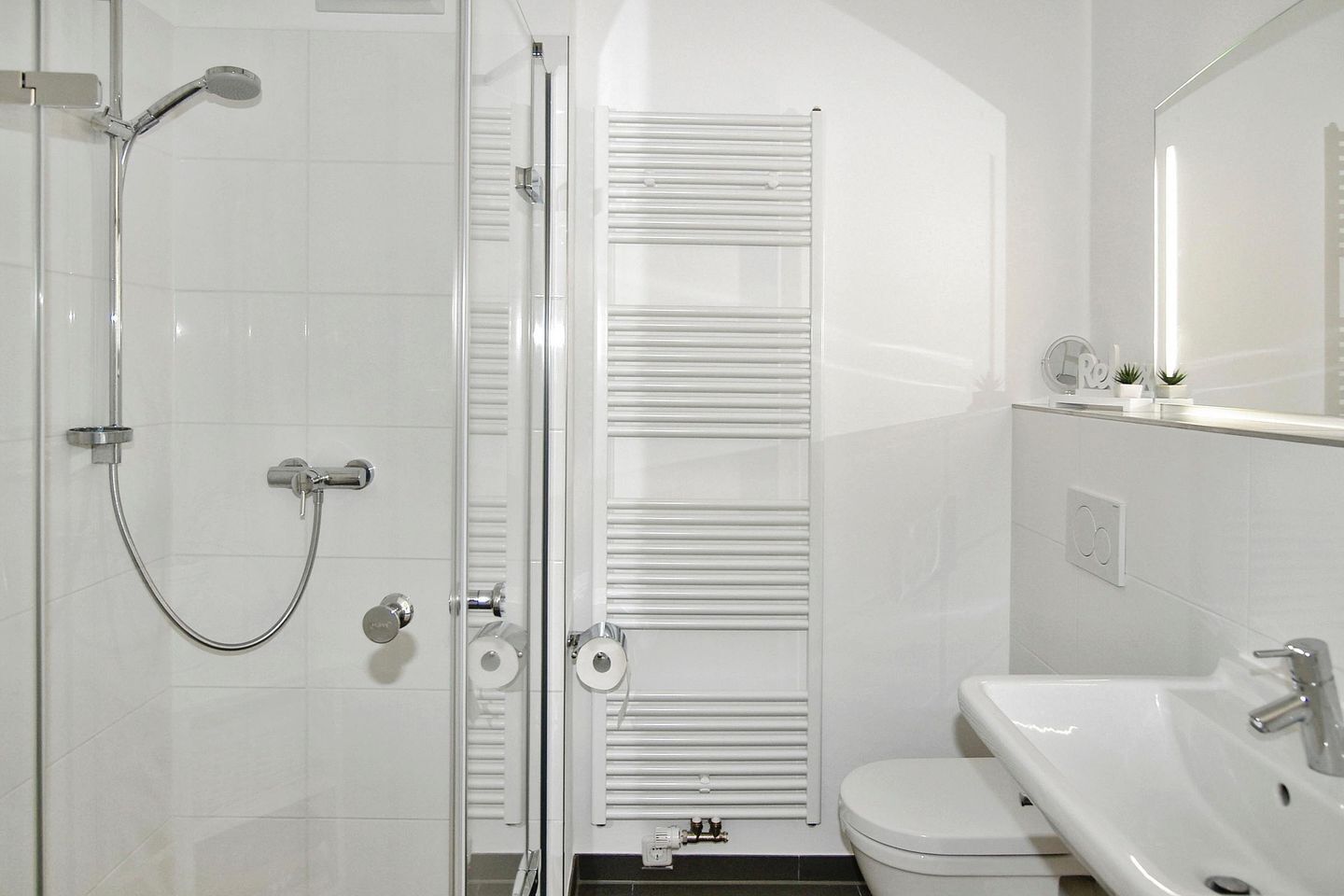 Une salle de bain moderne avec une douche à parois de verre, des toilettes blanches et un lavabo avec un miroir au-dessus.