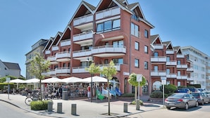 Een meerlaags woongebouw met balkons, een markt op de begane grond en geparkeerde auto's.