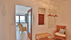Ein Zimmer mit einem Korbstuhl, einem kleinen Holztisch und einem Kleiderständer mit Kleiderbügeln.