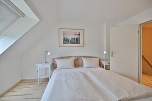 Quarto com uma cama, duas mesas de cabeceira com luminárias, um quadro na parede e uma porta à direita.