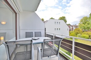 Uma varanda com mesa e cadeiras, vista para uma área residencial com casas e vegetação.