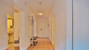 A hallway with a bench, a door, and a visible bathroom with a sink and mirror. - Sandpiper Apartment 2 - Sandpiper (Scharbeutz)