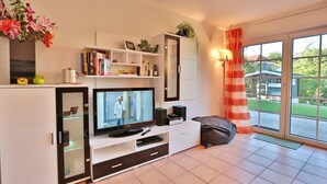 A modern living room with a flat-screen TV, a sofa, a coffee table, and a sliding glass door to a balcony. - Sandpiper Apartment 2 - Sandpiper (Scharbeutz)