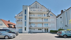 Un immeuble résidentiel à plusieurs étages, doté de balcons, d’un espace de stationnement et surplombant un ciel dégagé.
