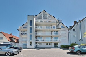 Un immeuble résidentiel à plusieurs étages, doté de balcons, d’un espace de stationnement et surplombant un ciel dégagé.