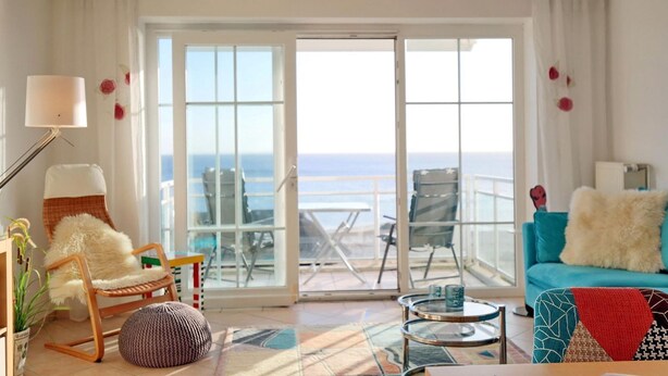 Un salon spacieux avec vue sur la mer, comprenant un canapé, des fauteuils, une lampe et une table basse.