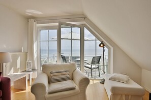 A modern living room with a large window overlooking the sea, a sofa, a small table, and a lamp.