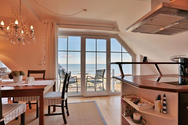 A modern kitchen with a view of the sea, a dining area with chairs, and a chandelier.