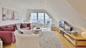 Ein modernes Wohnzimmer mit großem Fenster, Flachbildfernseher und Essbereich mit Meerblick.