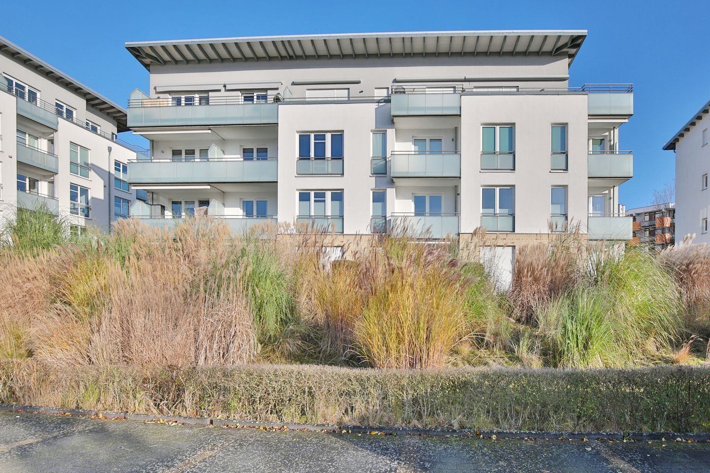 Un immeuble résidentiel moderne à plusieurs étages, doté de balcons et entouré d’une végétation luxuriante.