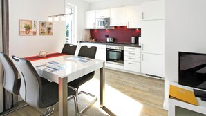 A modern kitchen with white cabinets, a microwave, an oven, and a coffee maker. There is a dining table with chairs and a small TV on a stand. - Strandglück, Apartment 8c - Strandglück House B (Scharbeutz)