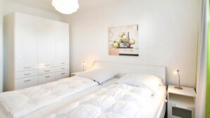 A bedroom with a double bed, a wardrobe, a bedside table with a lamp, and a wall-mounted artwork. - Strandglück, Apartment 8c - Strandglück House B (Scharbeutz)