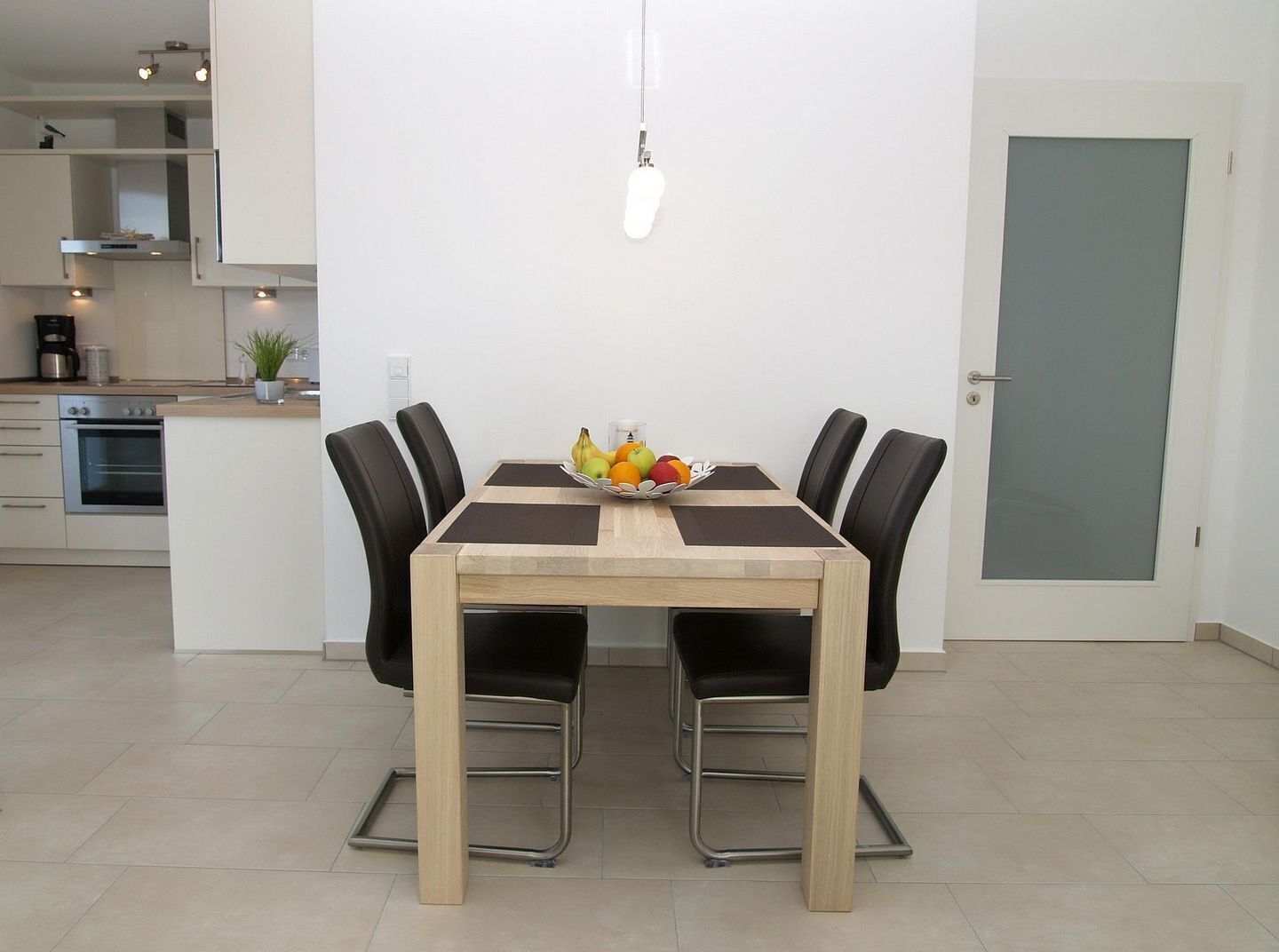 A dining area with a wooden table, black chairs, and a fruit bowl.
