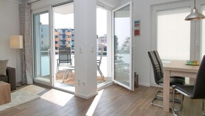 Un apartamento moderno con suelo de madera, zona de comedor con mesa y sillas, y balcón con vistas a edificios.
