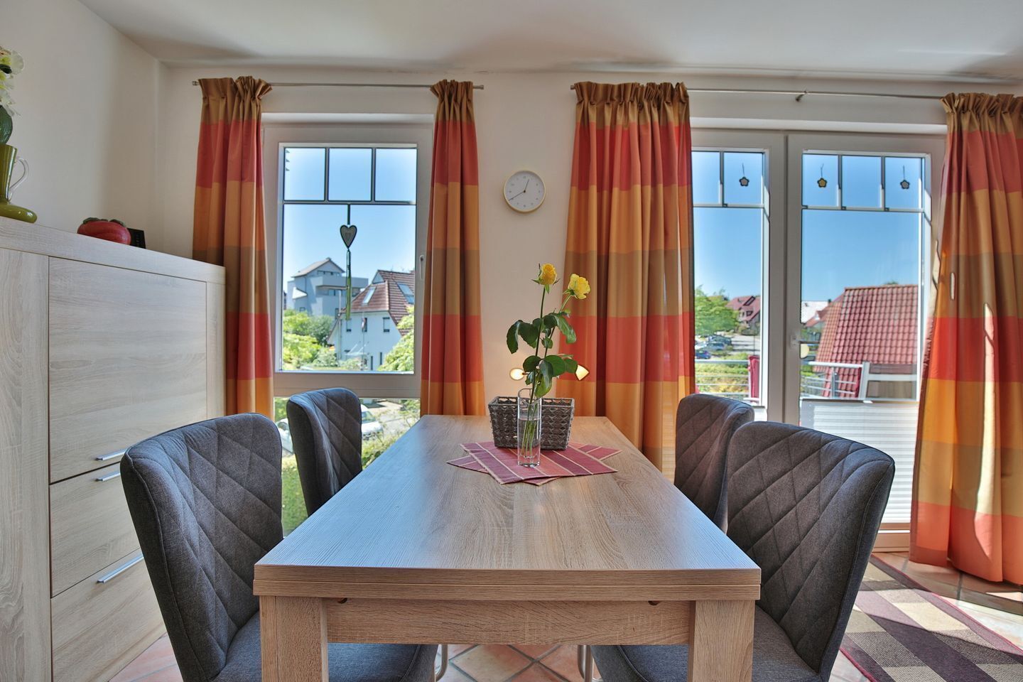 Un coin repas avec une table en bois, quatre chaises et une vue sur l’extérieur grâce à de grandes fenêtres.