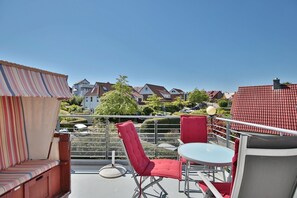 A balcony with a striped awning, red cushioned chairs, and a small table.
