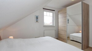 Un dormitorio con techo inclinado, un ventanal grande, una cama, un espejo y un radiador.