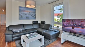 A modern living room with a sectional sofa, a flat-screen TV, and a large window with curtains.