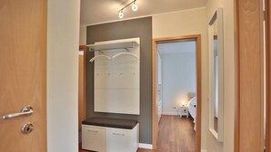 A modern hotel room with a wooden floor, a built-in bench with storage drawers, a large mirror, and a wardrobe with hanging space.