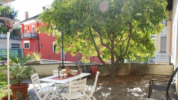 Eine Terrasse im Freien mit Tisch und Stühlen, umgeben von Blumentöpfen und einem Baum.