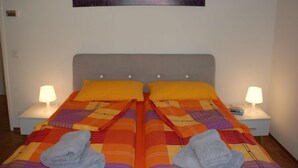 Ein Doppelbett mit einer farbenfrohen Steppdecke, zwei Kissen und zwei Nachttischlampen, über dem Bett hängt ein Gemälde.