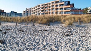 A beachfront hotel with multiple floors, a sandy beach in the foreground, and a clear sky.