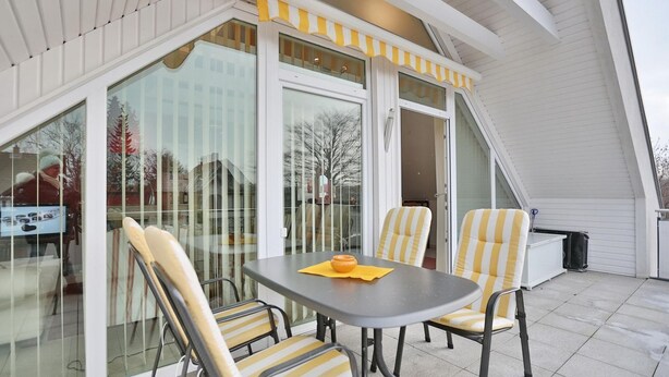 Een terras buiten met een tafel en stoelen, grote schuifdeuren en een geel gestreepte luifel.