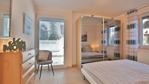A bedroom with a bed, a chair, a dresser, and a window with blinds. - Residenz Seeschwalbe Appartement 4 - Residenz Seeschwalbe (Scharbeutz)