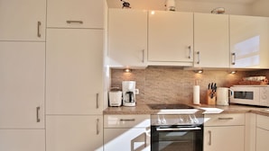 A modern kitchen with white cabinets, a built-in oven, a coffee maker, and a microwave. - Residenz Seeschwalbe Appartement 4 - Residenz Seeschwalbe (Scharbeutz)