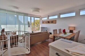 A modern living room with a sofa, dining table, and a staircase with a railing.