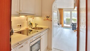 A kitchen with white cabinets, a double sink, and an oven. There is a window with curtains and a view of the outside. - Seesternresidenz Apartment 15 - Seesternresidenz (Scharbeutz)
