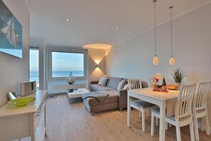 Una sala de estar moderna con un sofá, una mesa de comedor y sillas. Se ve un ventanal con vista al mar.