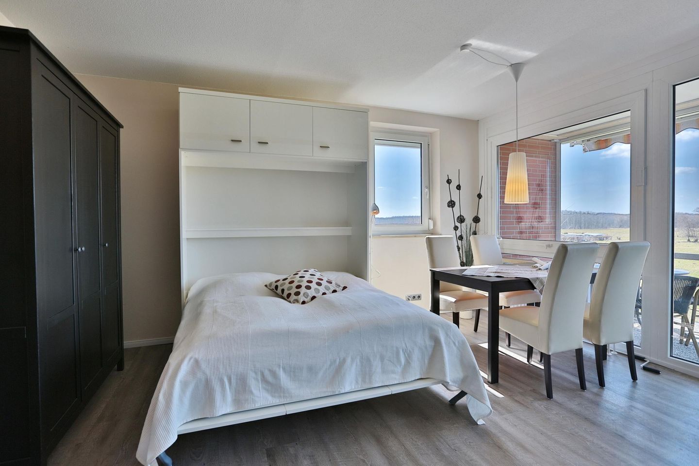 A bedroom with a bed, a desk, chairs, and a large window with a view.