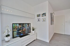 A modern living room with a flat-screen TV on a white console, a potted plant, and a door to the right. - Nautica Apartment 11 Bettina - House Nautica (Scharbeutz)