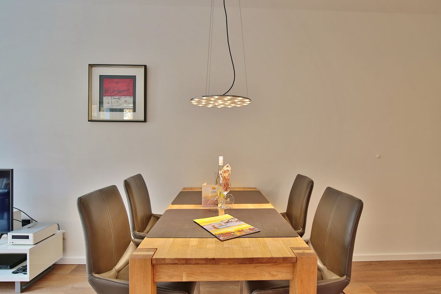 A dining area with a wooden table, leather chairs, a hanging light fixture, and a framed picture on the wall.