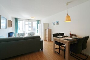 Un salon moderne comprenant un canapé, une table à manger et des chaises, un téléviseur et une fenêtre avec des rideaux.