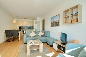 Un salon moderne avec un canapé, une table basse, un téléviseur et une cuisine en arrière-plan.