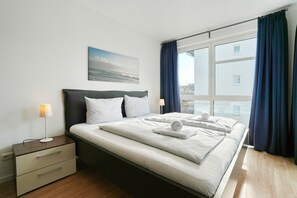 Une chambre d’hôtel avec un lit, des tables de chevet, une fenêtre avec des rideaux et un tableau au mur.