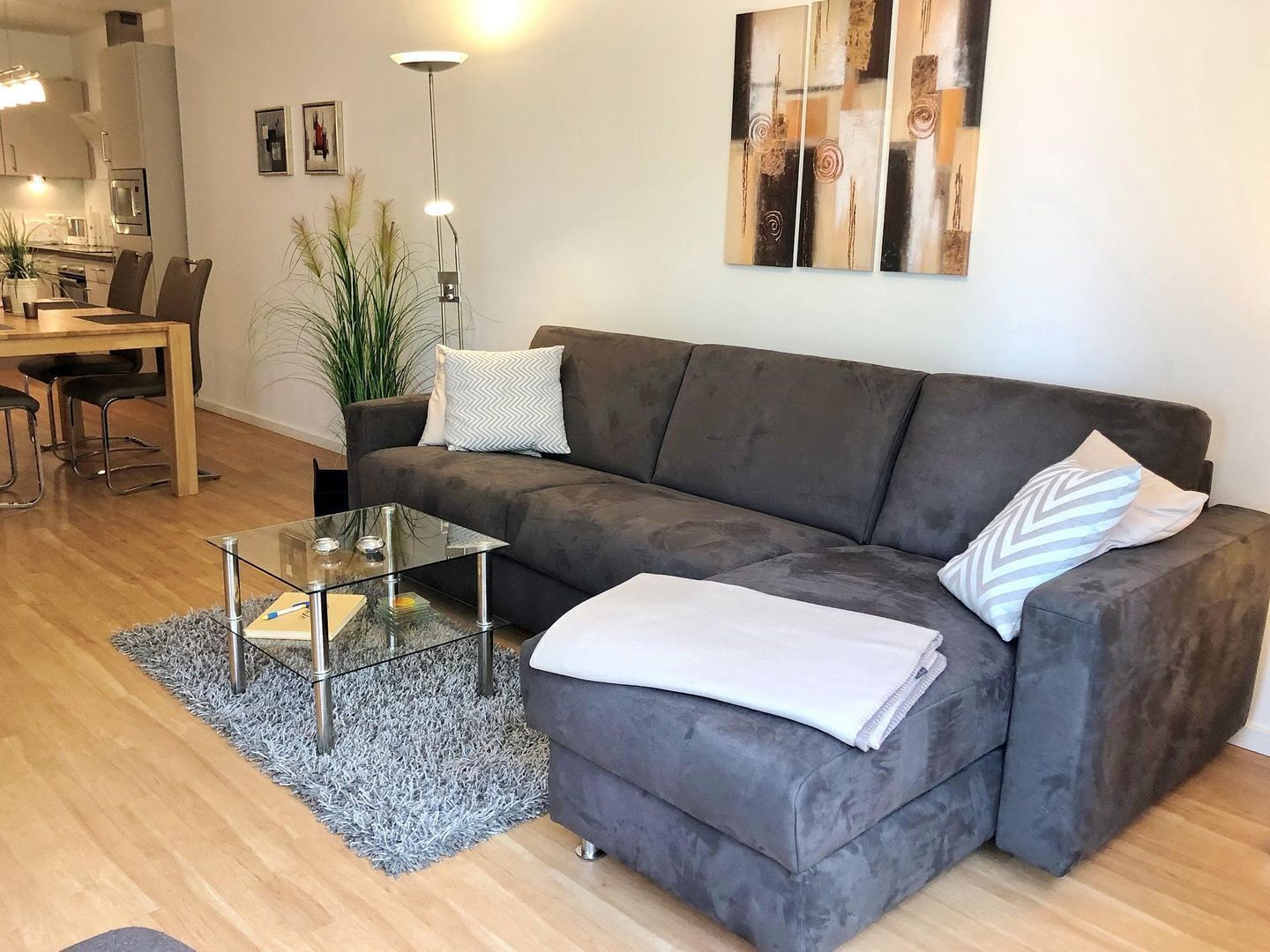 A modern living room with a grey sofa, a glass coffee table, and a dining area with a wooden table and chairs.