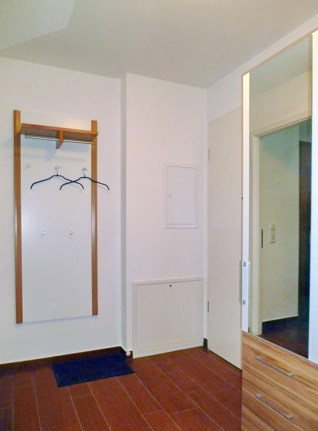 Una habitación con un armario de madera, un radiador y una puerta con espejo.